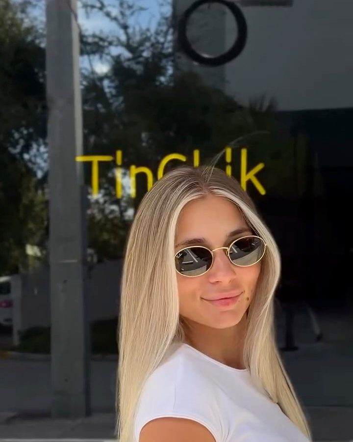 Blonde client with long wavy hair and sunglasses in front of the TinChik sign