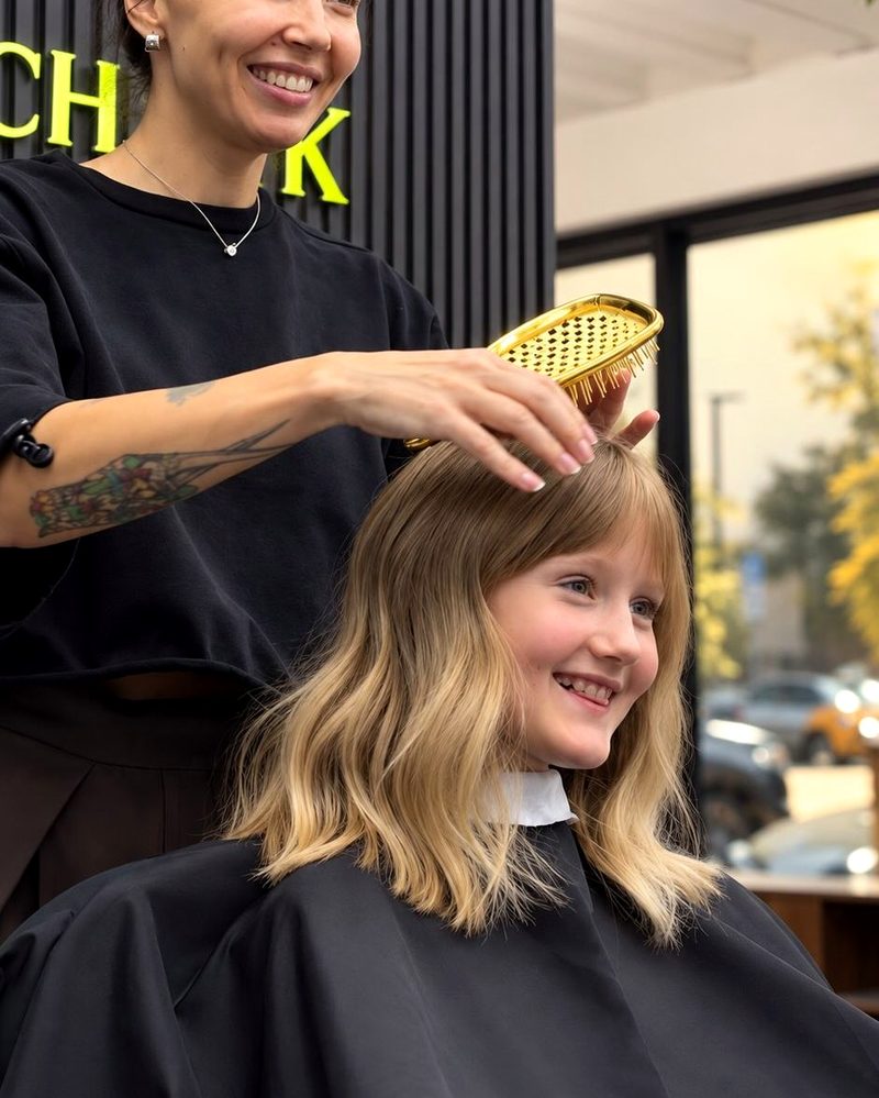 Tina cutting a young client's blonde hair, both of them smiling