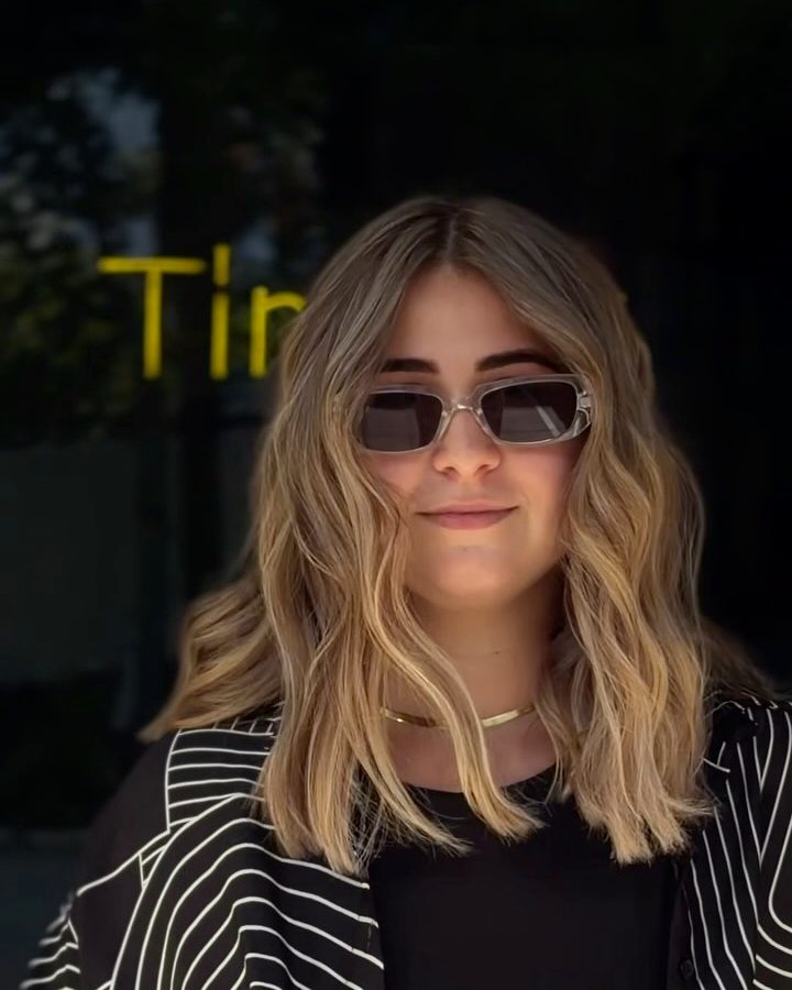 Client with long blonde AirTouch waves and sunglasses, smiling outside the salon