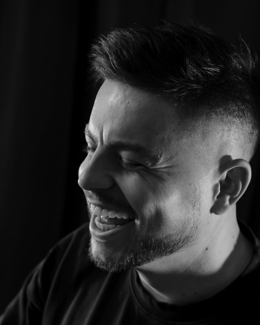 Black and white portrait of a client laughing, showing a clean skin fade and trimmed beard